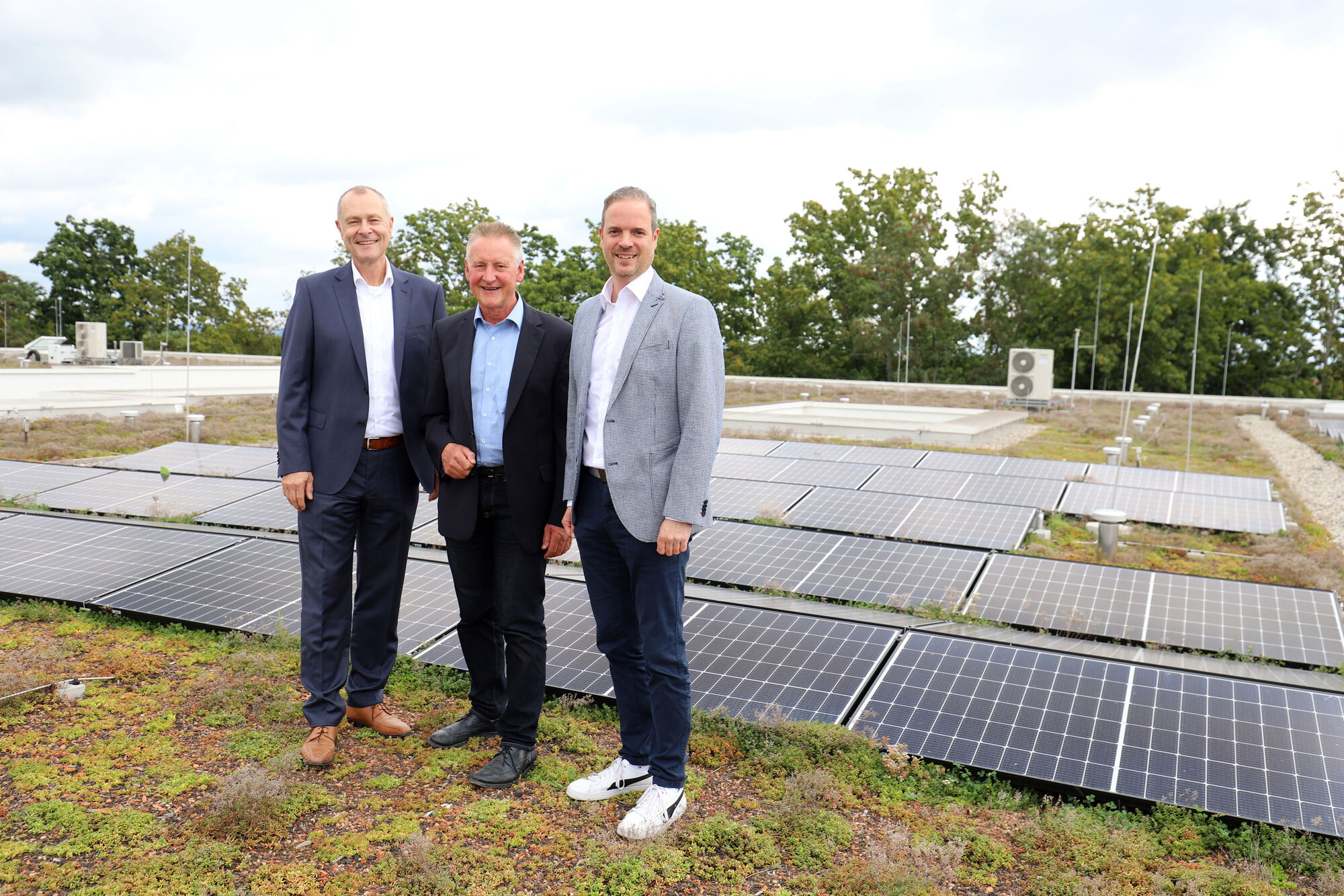 Dr. Matthias Keilen und zwei Mitarbeitende vor der PV-Anlage auf dem Dach der Klinik für Psychiatrie und Psychotherapie Fürth